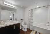 Thumbnail 26 of 28 - Pet Friendly Apartments in Hollywood CA - The Fifty Five Fifty - A Spacious Bathroom With White Countertops, Dark Cabinetry, Wood-Style Flooring, And A Full Shower/Tub Combo