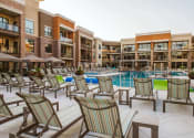 Thumbnail 5 of 75 - Rows of chaise lounge chairs around an outdoor pool surrounded by apartment buildings at The Apex at CityPlace, Kansas, 66210