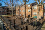 Thumbnail 6 of 16 - a fenced in area with a bench and trees in front of a brick building