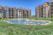 Thumbnail 21 of 78 - a fountain in the middle of a grassy area with an apartment complex in the background  at EdgeWater at City Center, Lenexa, 66219