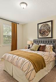 A bedroom with a large bed and a decorative plant on a table.