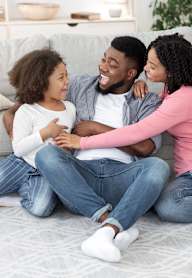 A family of three is sitting on the floor in a living room.
