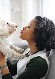 A woman is kissing a white dog on the cheek.