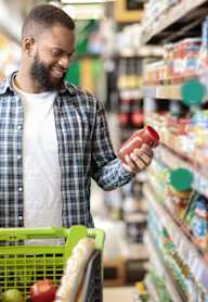 A woman is shopping in a grocery store with a basket of fruits and a tablet.