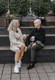 Two people sitting on a bench, one holding a cup.