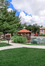 a park with a pool and a gazebo and trees with a building