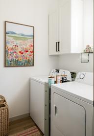 A laundry room with a washer and dryer, a basket, and a painting of flowers on the wall.