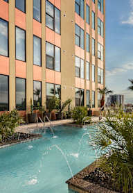 A pool with a waterfall in front of a building with a balcony.