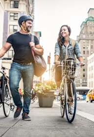 A man and a woman are walking down the street with bicycles.