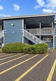 A parking lot in front of a blue building with a staircase leading to the entrance.