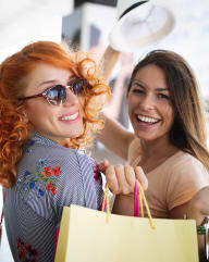 three women holding shopping bags and smiling at the camera