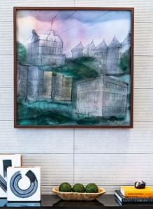 a painting hanging on a wall above a table with a desk and a shelf
