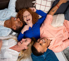 Four people lying on a couch, smiling and laughing together.