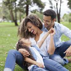 A family of three is sitting on the grass in a park.