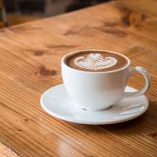 A cup of coffee with a latte art on top is placed on a saucer.
