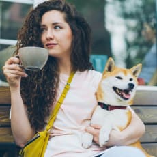 a woman sitting on a bench with a dog and a cup of coffee