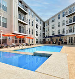 A swimming pool surrounded by apartment buildings and lounge chairs.