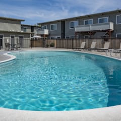 a swimming pool with chairs around it in front of an apartment building