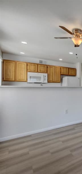 a living room with a ceiling fan and a kitchen in the background