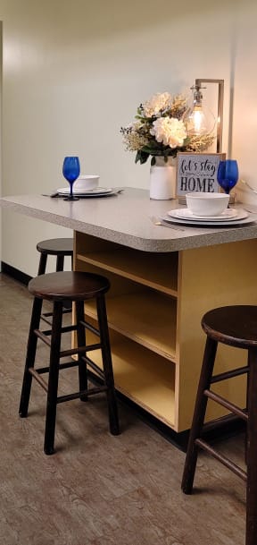 a kitchen counter with three stools and a table with a vase of flowers
