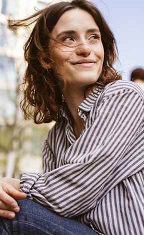 A woman in a striped shirt is sitting on a ledge.