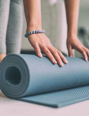 A person is rolling up a blue yoga mat.