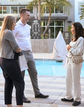Three people are standing by a pool and having a conversation.