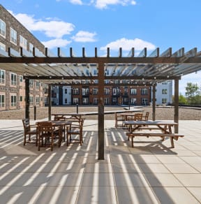 a pergola with tables and chairs on a patio in front of a brick building