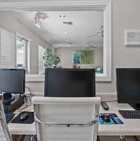 Three monitors are on a desk with a white chair.