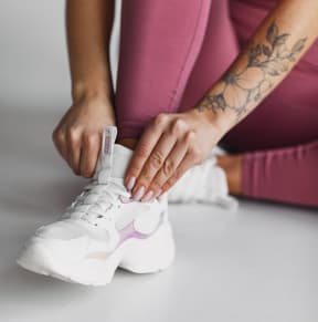 close up of a woman tying shoelaces on white sneakers on the floor free photo