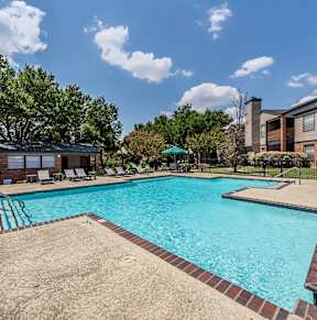 A large swimming pool surrounded by a sandy area and a few trees.