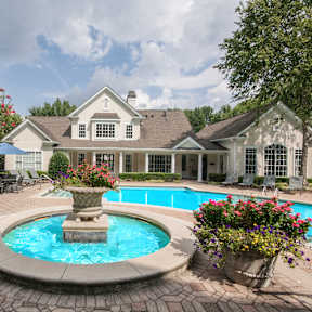 A large house with a pool and a fountain in the middle of a garden.