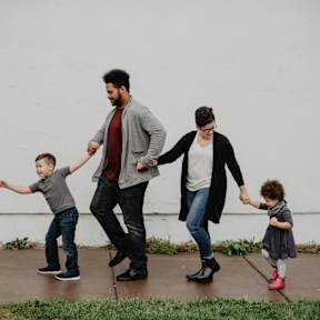 A family of four is walking together on a sidewalk.