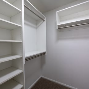 a spacious closet in a bedroom with white shelves and a window