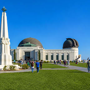 A monument stands in front of a large building with two domes.