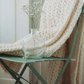 A glass vase with baby's breath flowers sits on a green glass table.