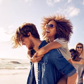 A man is carrying a woman on his back on a beach.