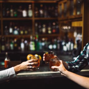 two people holding their drinks at a bar