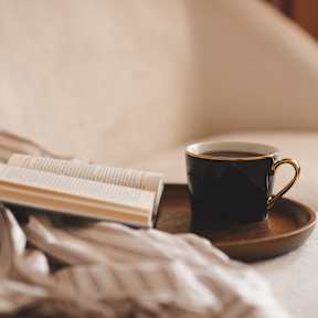 A cup of coffee and an open book on a bedside table.