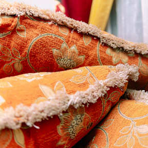A close up of a red and orange floral patterned pillow with frayed edges.
