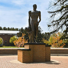 A statue of a man holding a hat is on a brick pedestal.