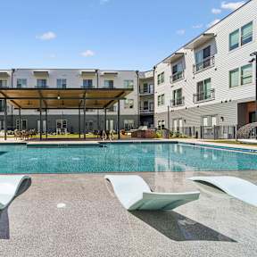 A swimming pool with sun loungers in front of apartment buildings.