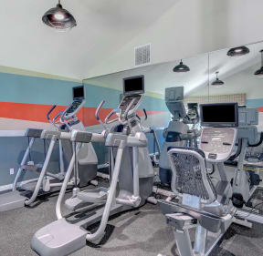 four exercise machines in a gym with a wall with an orange stripe