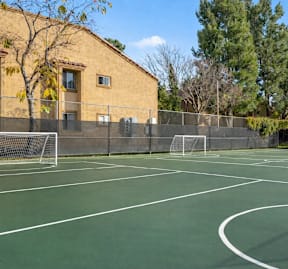 A tennis court with a green surface and white lines, surrounded by a chain link fence.