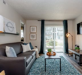 A living room with a grey couch, a coffee table, and a flat screen TV mounted on the wall.