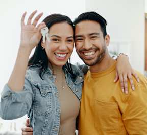 A man and woman are standing close together, smiling and waving.