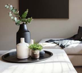 A black vase with a plant in it sits on a tray on a white couch.