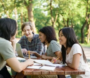 a group of people sitting at a picnic table looking at a laptop