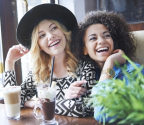 two women sitting at a table in a cafe with drinks