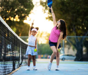 a woman and a little girl playing tennis on a tennis court